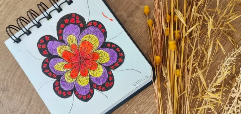 Fotografia em tons pastel e terracota, apresentando o título 'Clareza Emocional e Reorganização Energética: Atividades Manuais como Meio de Chegar ao Inconsciente'. A imagem mostra mãos segurando um pincel e colorindo uma flor estilizada (uma mandala botânica) em um caderno de anotações com espiral, representando a prática clínica e o autoconhecimento inspirado em Jung. Ao redor, há elementos simbólicos como tintas, tecidos e uma referência ao Human Design, ilustrando o processo de autodescoberta e cura.